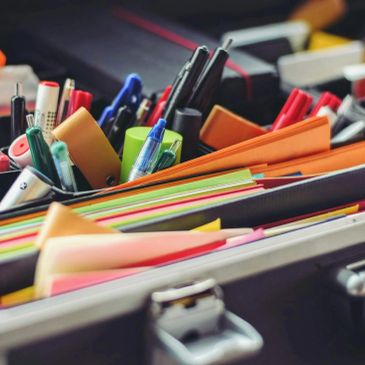 Open briefcase filled with colorful stationery and writing tools.