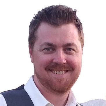 Smiling man with beard wearing a white shirt and dark vest.