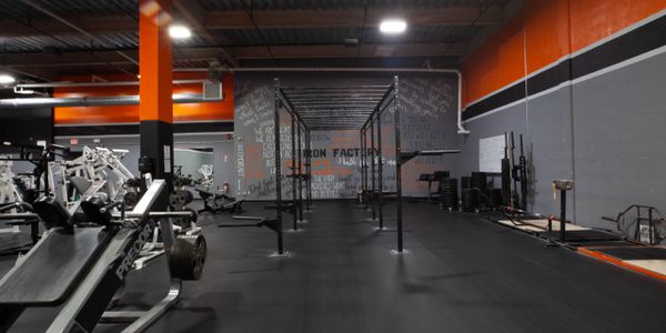 orange and grey wall with high ceiling containing workout equipment plus squat rack