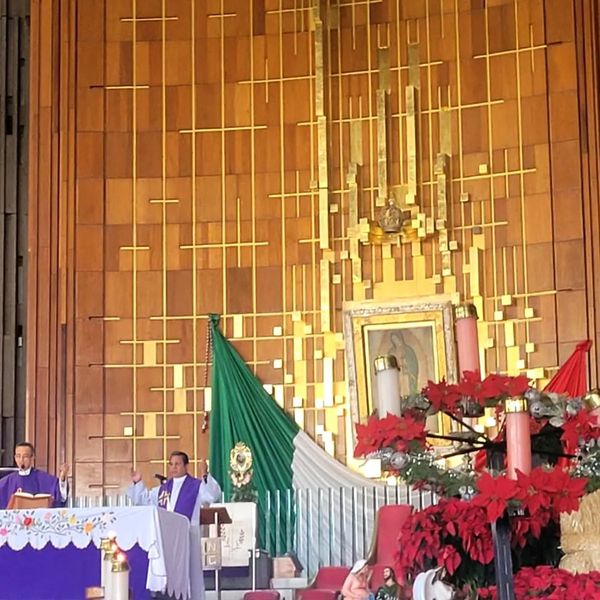 Catholic mass with priests, Mexican flag, and poinsettia decorations inside a church.