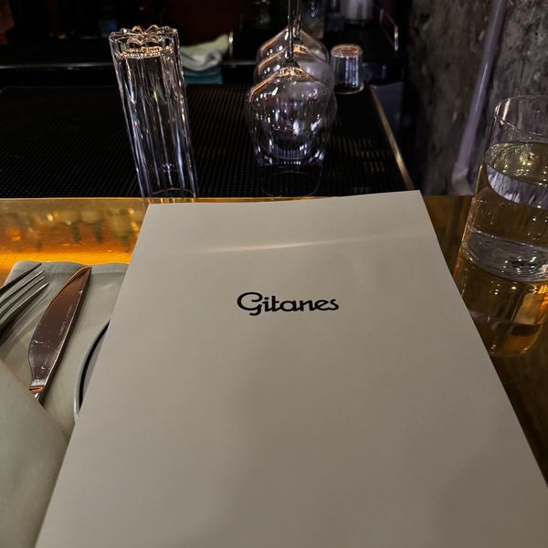 A restaurant menu labeled 'Gitanes' on a table set with utensils and a glass of water.