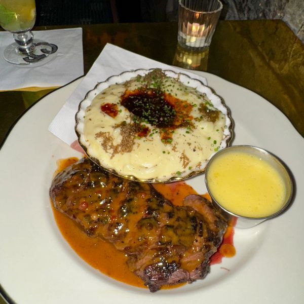 Grilled steak with mashed potatoes and a creamy sauce on a white plate.