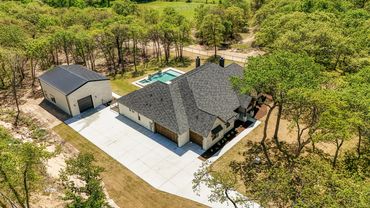 Aerial view of a modern house with a pool, garage, and surrounding trees.