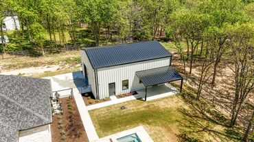 A modern metal shed with a black roof and white walls beside a house.