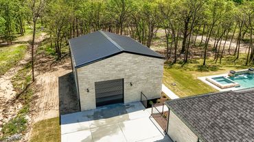 Stone building with a metal roof next to a pool and wooded area.