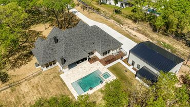 A modern house with a swimming pool and a large detached garage surrounded by trees.