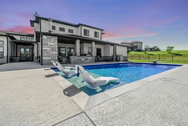 Modern house with a pool and lounge chairs under a purple sunset sky.