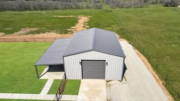 A modern metal barn with a carport in a rural green field.