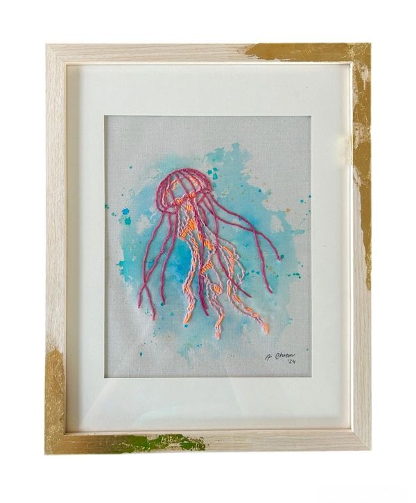 Framed embroidered jellyfish art with blue watercolor background.