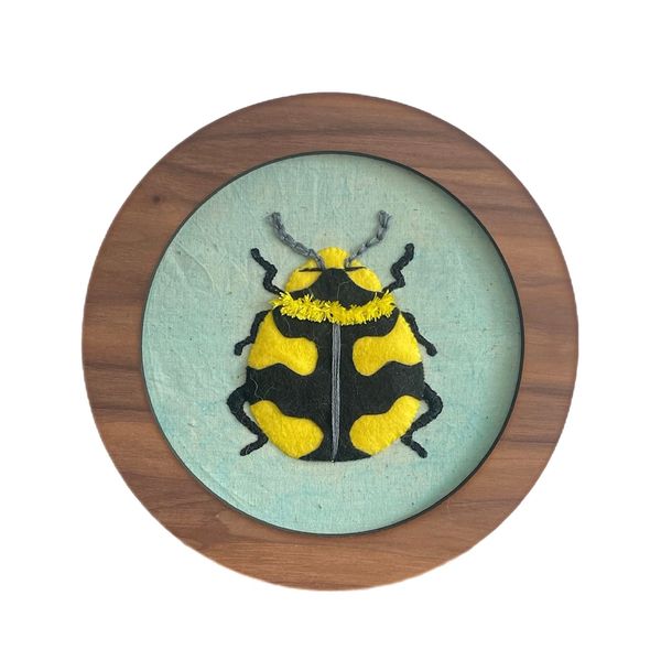Handcrafted felt bee art in a wooden frame.