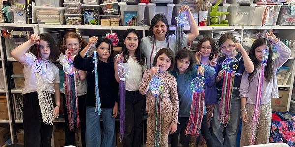 A group of children and an adult holding colorful lighted crafts in a craft room.