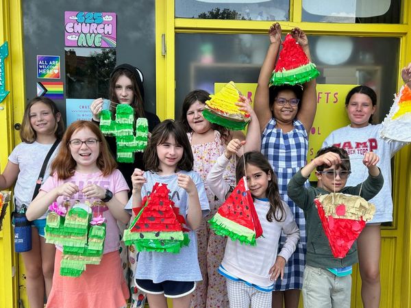 Group of children proudly holding handmade colorful piñatas outside a craft store.