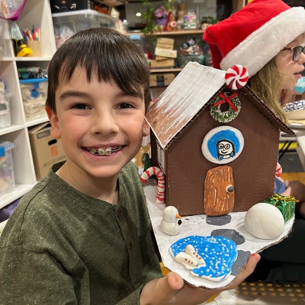 A smiling boy showing a festive handmade gingerbread house model.