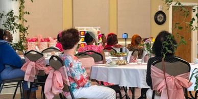 Women seated around tables in a decorated event hall, engaged in a gathering.