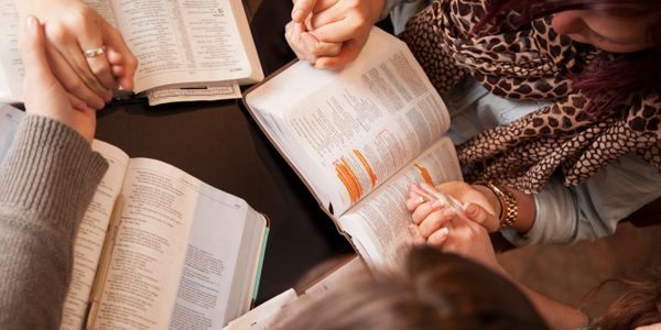 People holding hands in prayer around open Bibles with highlighted text.