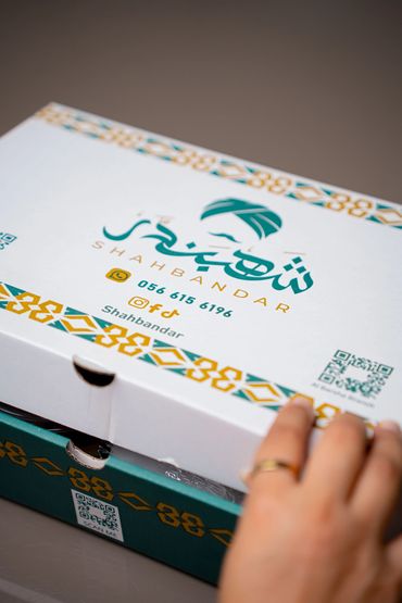Close-up of Shahbandar branded boxes with contact details and a hand opening one.