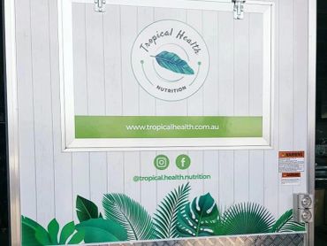 Signage for Tropical Health Nutrition with green leaf graphics and social media handles.