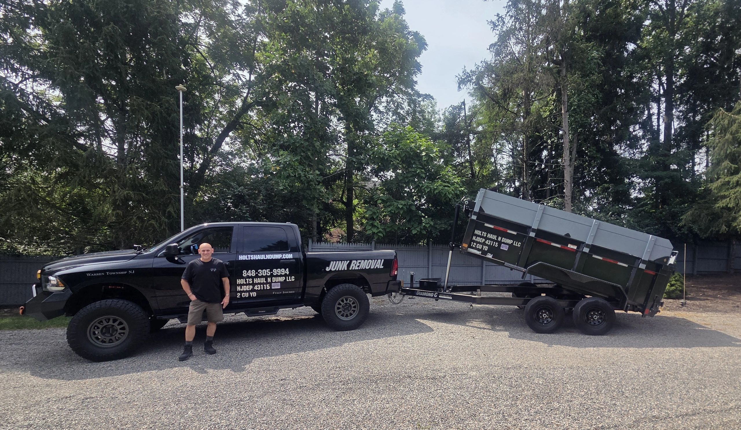 Man standing beside a black junk removal truck and trailer.