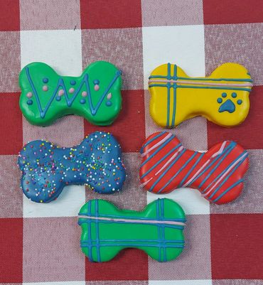 Colorful dog bone-shaped cookies with icing on a checkered tablecloth.