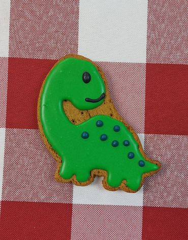 Green dinosaur-shaped cookie on red and white checkered cloth.