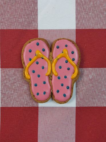 Cookie decorated like pink flip-flops with orange straps on red checkered cloth.
