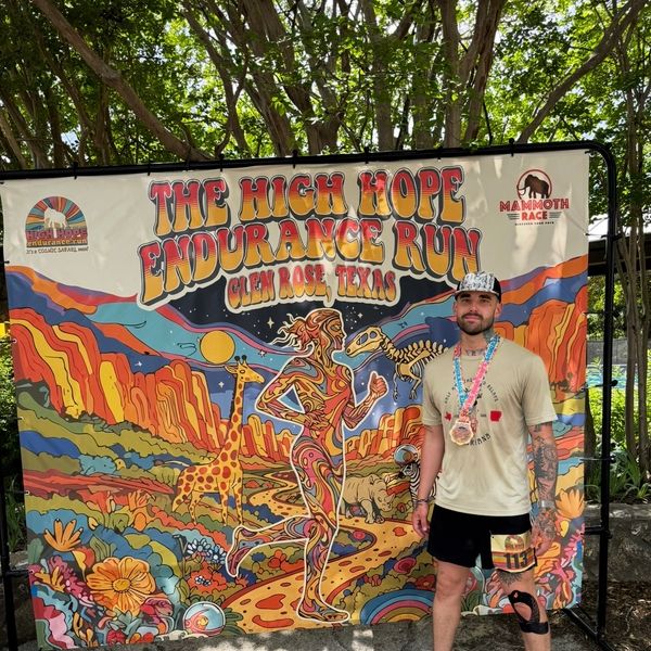 Man with medals stands in front of colorful High Hope Endurance Run banner.