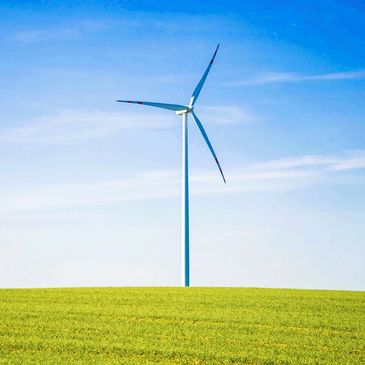 A single wind turbine standing on a green field under a clear blue sky.