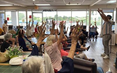 Senior group participating in a seated exercise session led by an instructor.