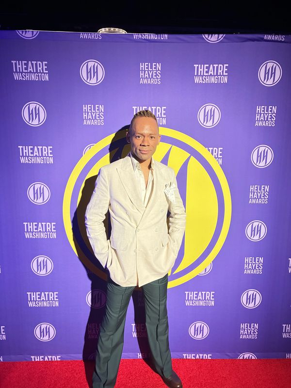 Man in white blazer and dark pants poses on red carpet at Helen Hayes Awards.