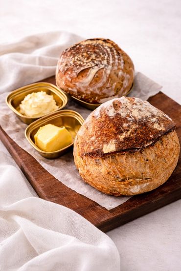 Two rustic bread loaves with butter and cream on a wooden board.