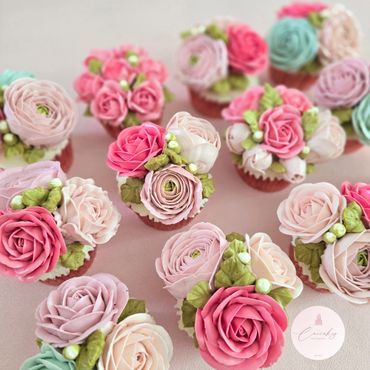 Cupcakes decorated with intricate pastel flower designs and green leaves.