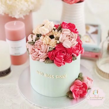 Elegant birthday cake adorned with intricate buttercream flowers in pink and red tones.
