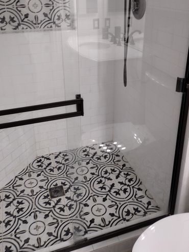 Modern shower with black and white patterned tiles and glass door.