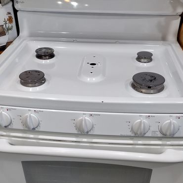 White gas stove with four burners and control knobs on the front panel.