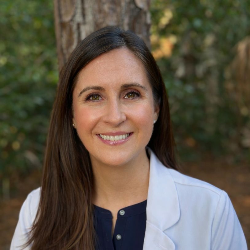 Smiling woman outdoors wearing a white coat.