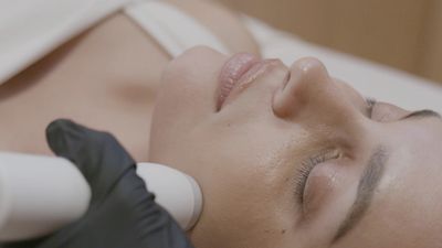 A woman receiving a facial treatment with a handheld device.