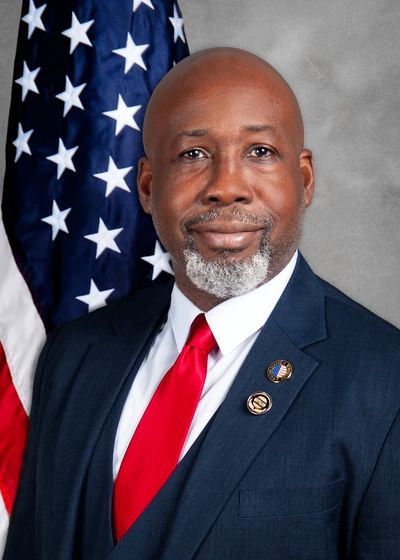 Portrait of a confident man in a suit with an American flag backdrop.
