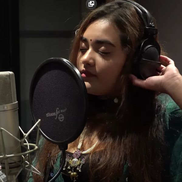 A woman singing passionately in a recording studio wearing headphones.