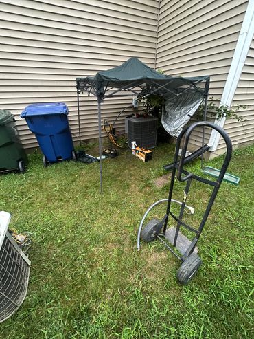 Backyard scene with HVAC unit and tools under a canopy.