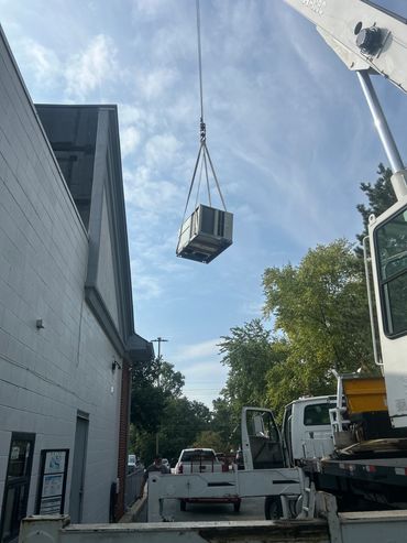 Crane lifting an HVAC unit near a building.