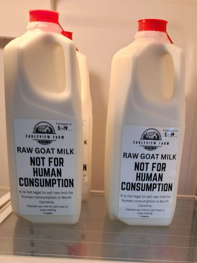 Bottles of raw goat milk labeled 'Not For Human Consumption' with red caps.