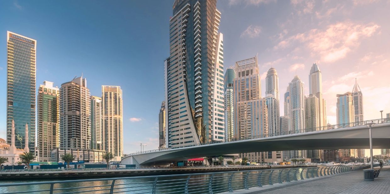 Modern skyscrapers and a bridge over calm water at sunset.