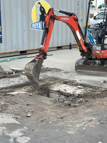 A Kubota excavator digging into concrete at a construction site.