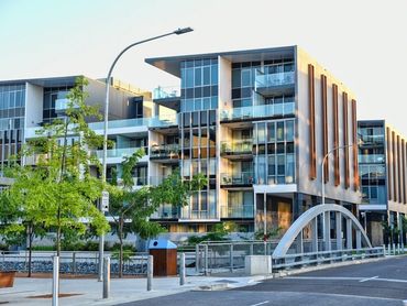 Modern apartment complex with glass balconies and greenery on a sunny day.