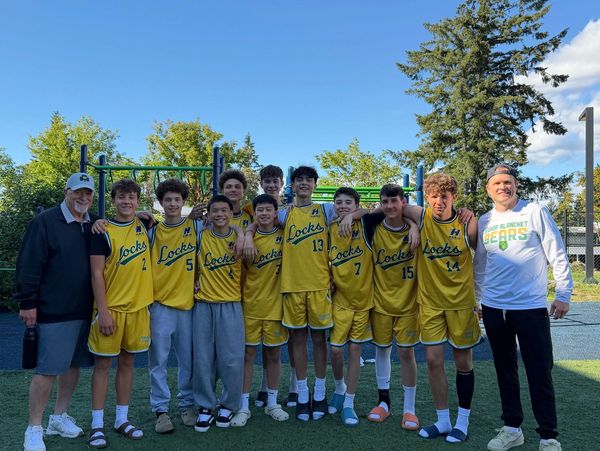 Youth basketball team in yellow uniforms posing outdoors with two coaches.