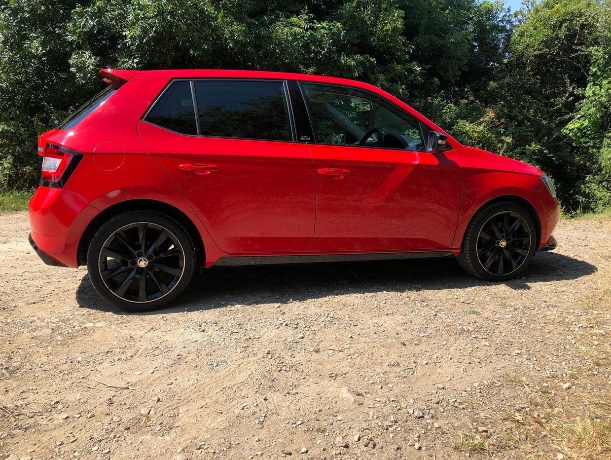 Red hatchback car parked on a dirt road.