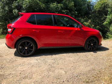 Red hatchback car parked on a dirt road.