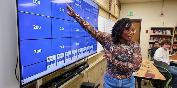 Teacher points at interactive board during class.