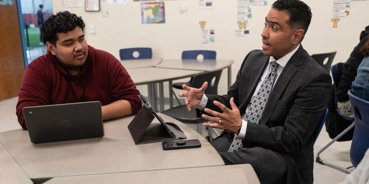 Teacher and student having a discussion at a table with laptops.