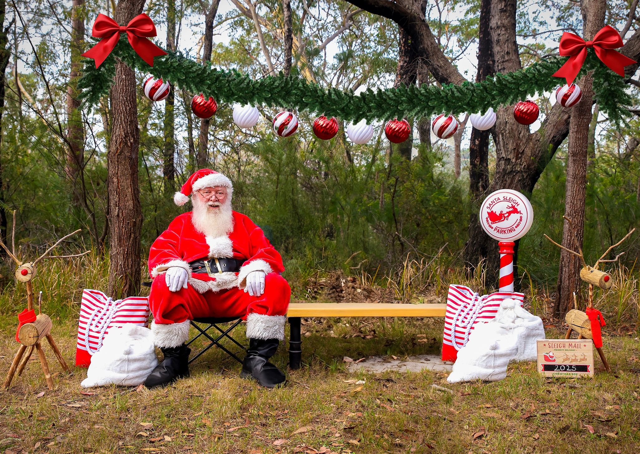 Santa Claus sitting on a bench in a festive outdoor setting with Christmas decorations.